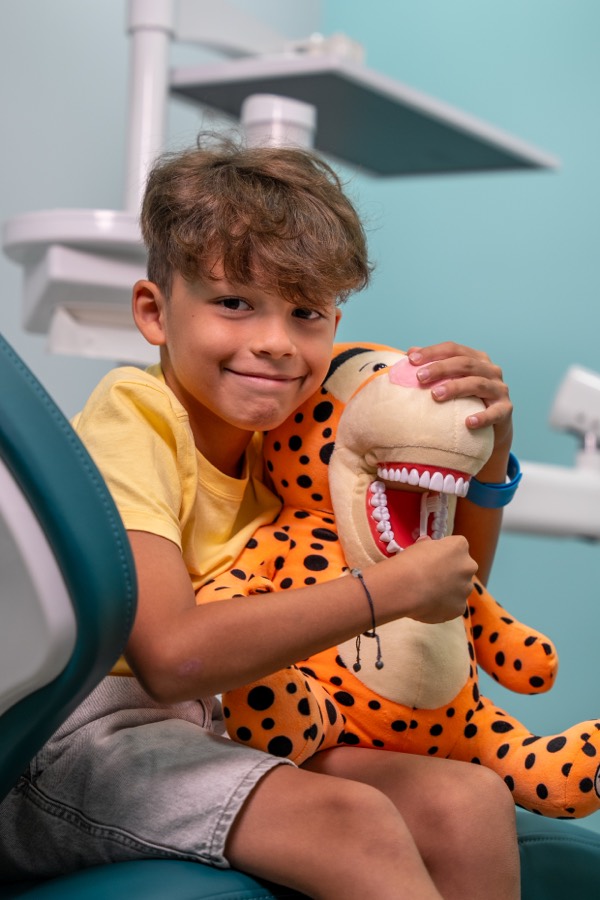 Niño feliz con peluche de tigre en el sillón dental